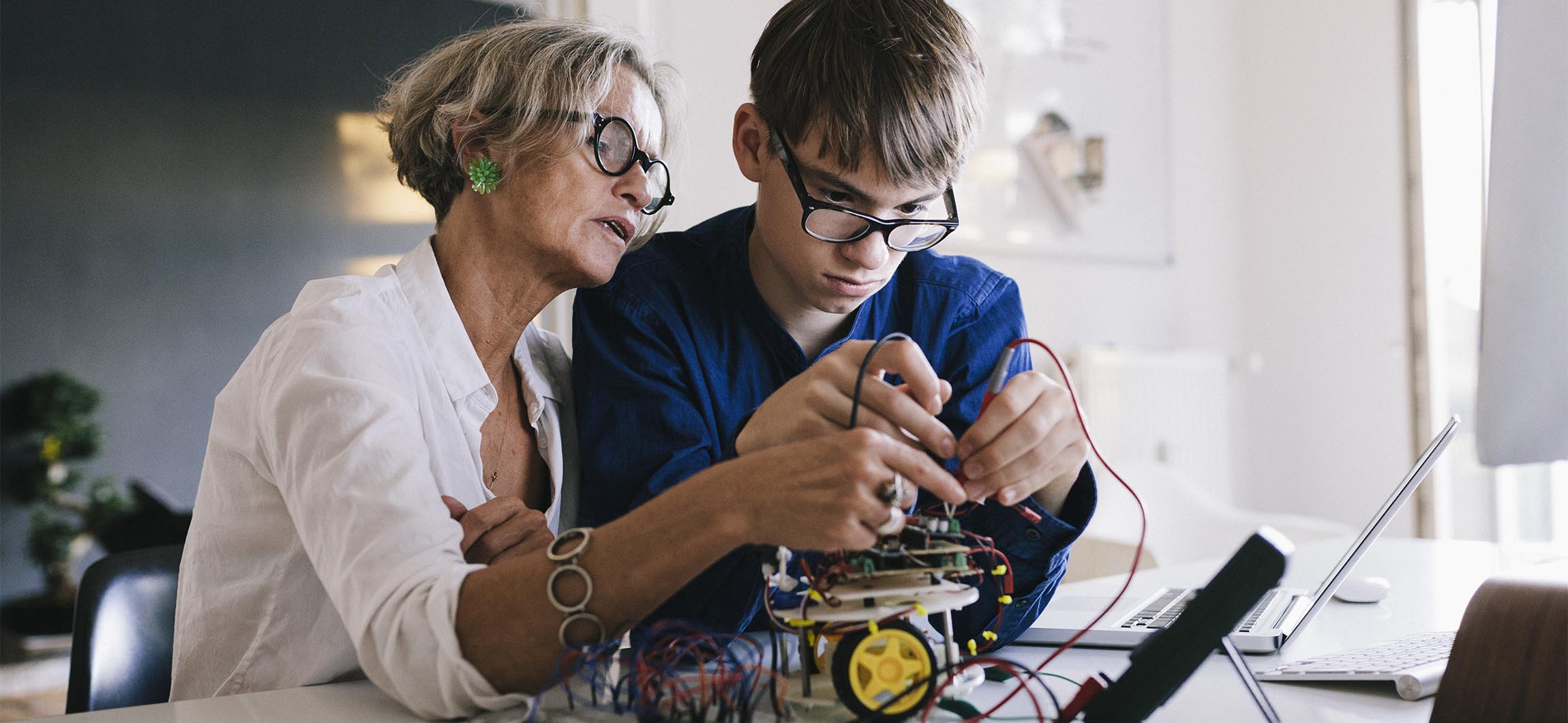 Mother and son working on electronic project together. Mother is showing son how to use voltage meter.