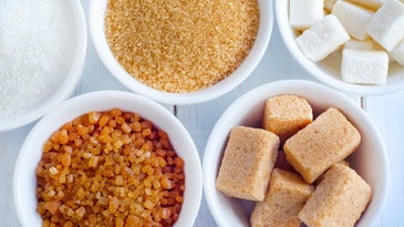 White bowls of white sugar, brown sugar, cane sugar, and unrefined sugar