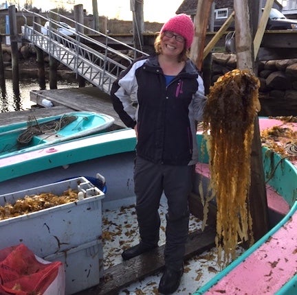 A woman holds a bunch of kelp on her boat.