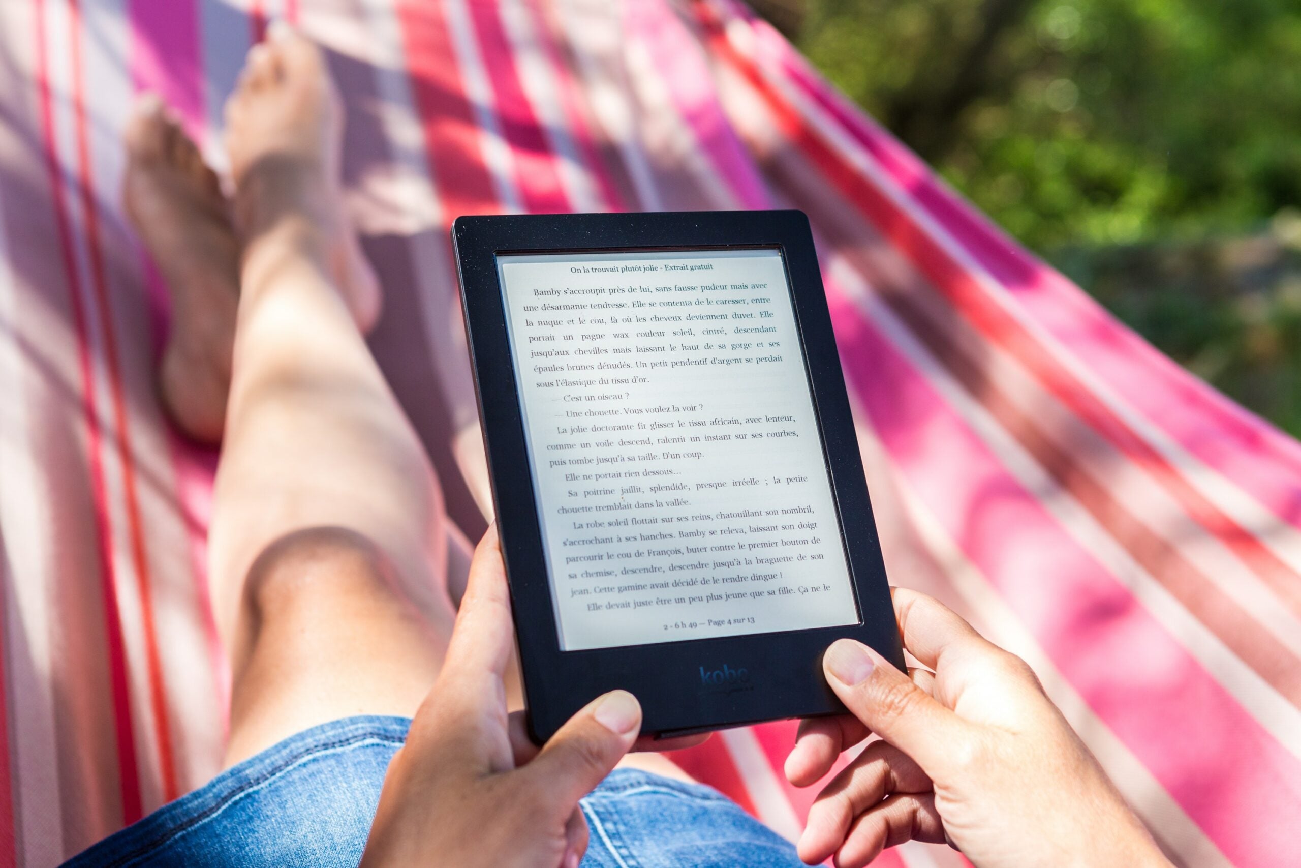 A person in a hammock outside, reading an e-book on a Kindle.