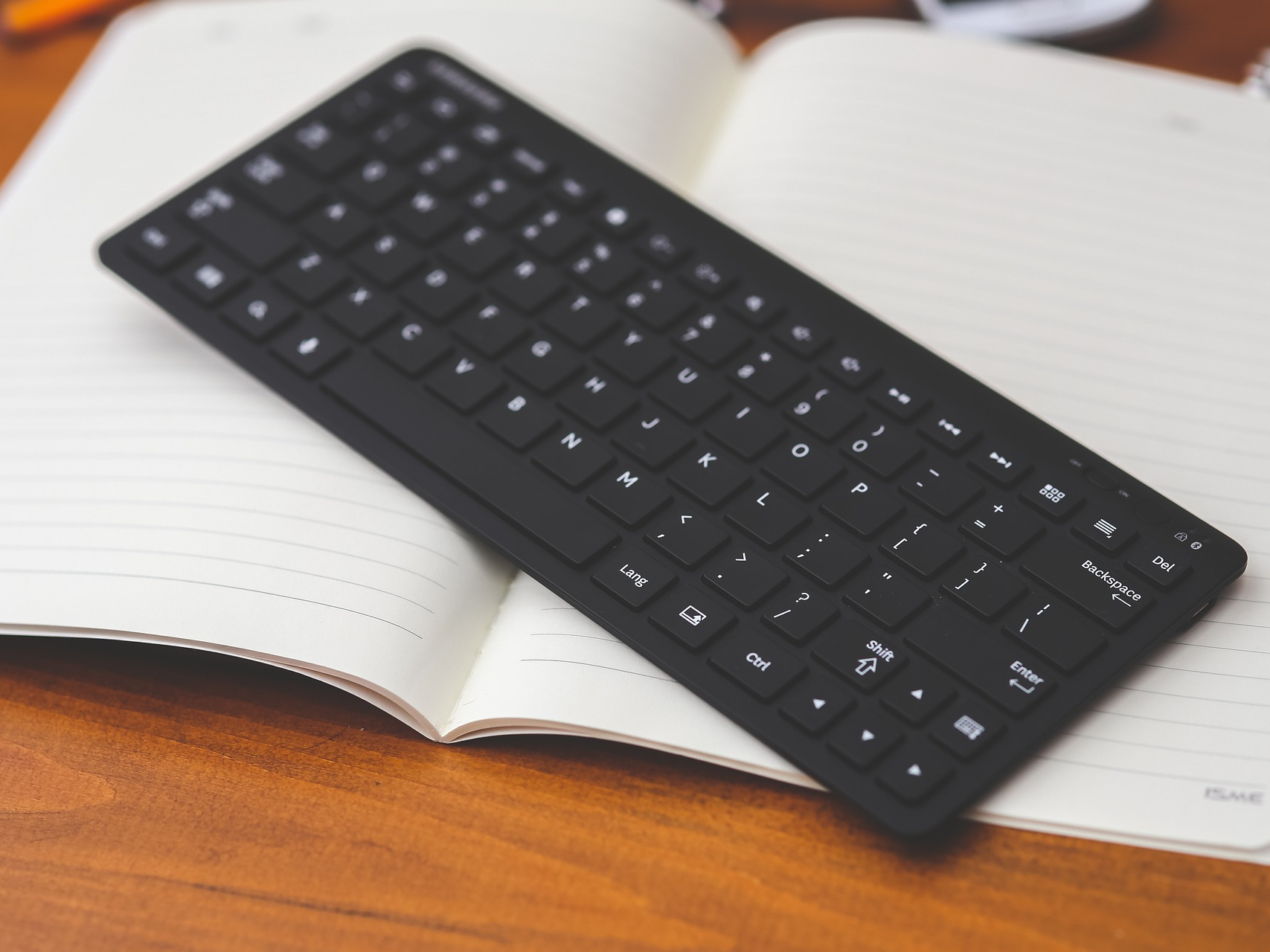 A black Bluetooth computer keyboard on an empty white notebook.