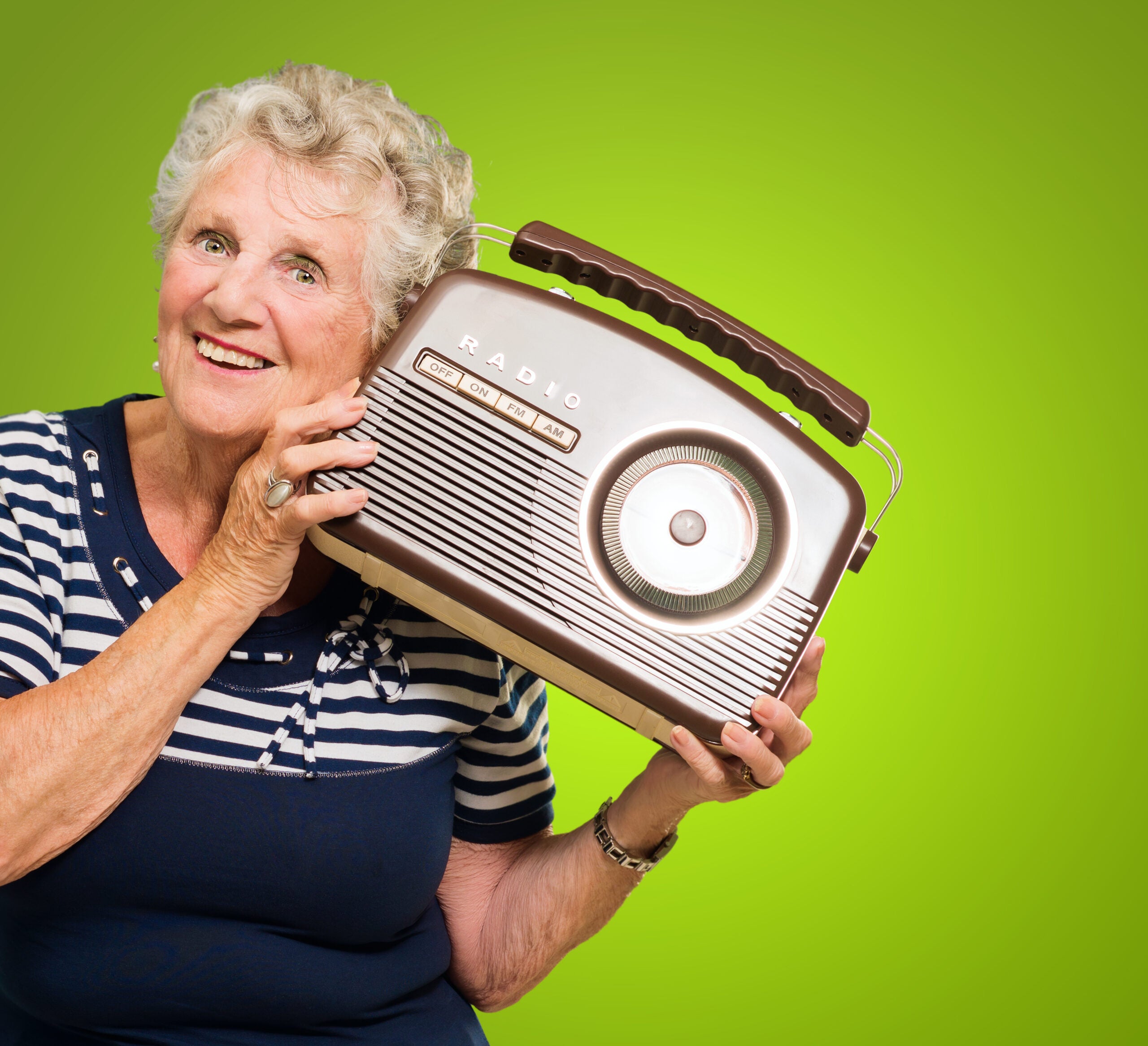 Senior woman holding an old radio to her ear and smiling.