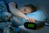 A woman snoozing an alarm clock at 6 a.m. in a dim room