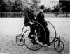 a couple in victorian clothing on an old-fashioned bicycle