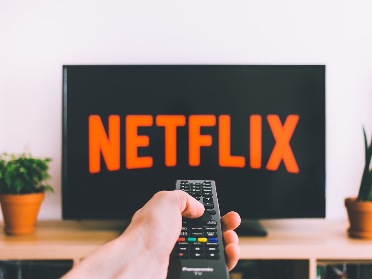 A person pointing a TV remote at a TV with Netflix on the screen. It's possible they're sharing a Netflix account with someone else.