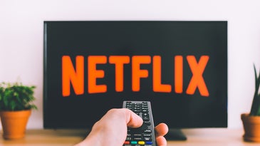 A person pointing a TV remote at a TV with Netflix on the screen.