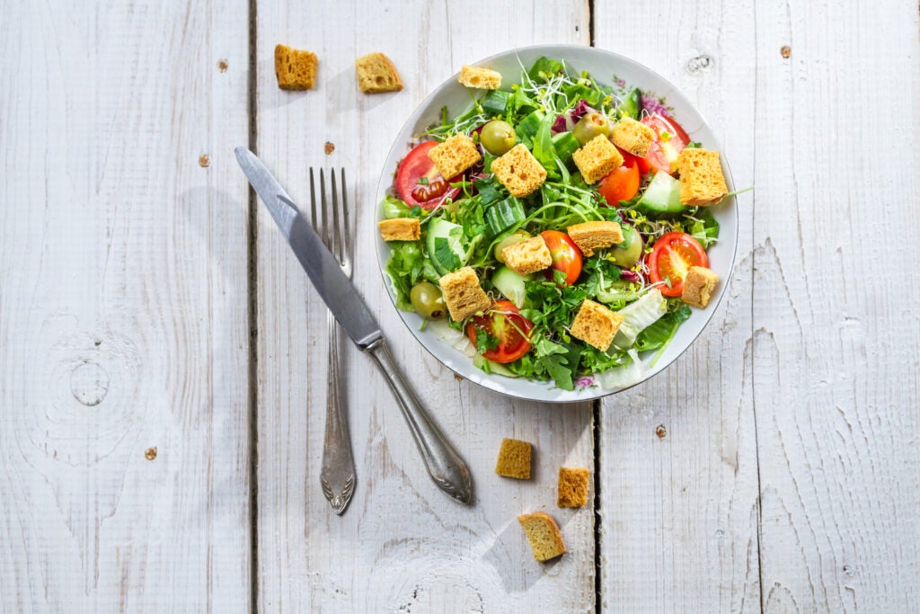 Bowl of salad with croutons over a white table