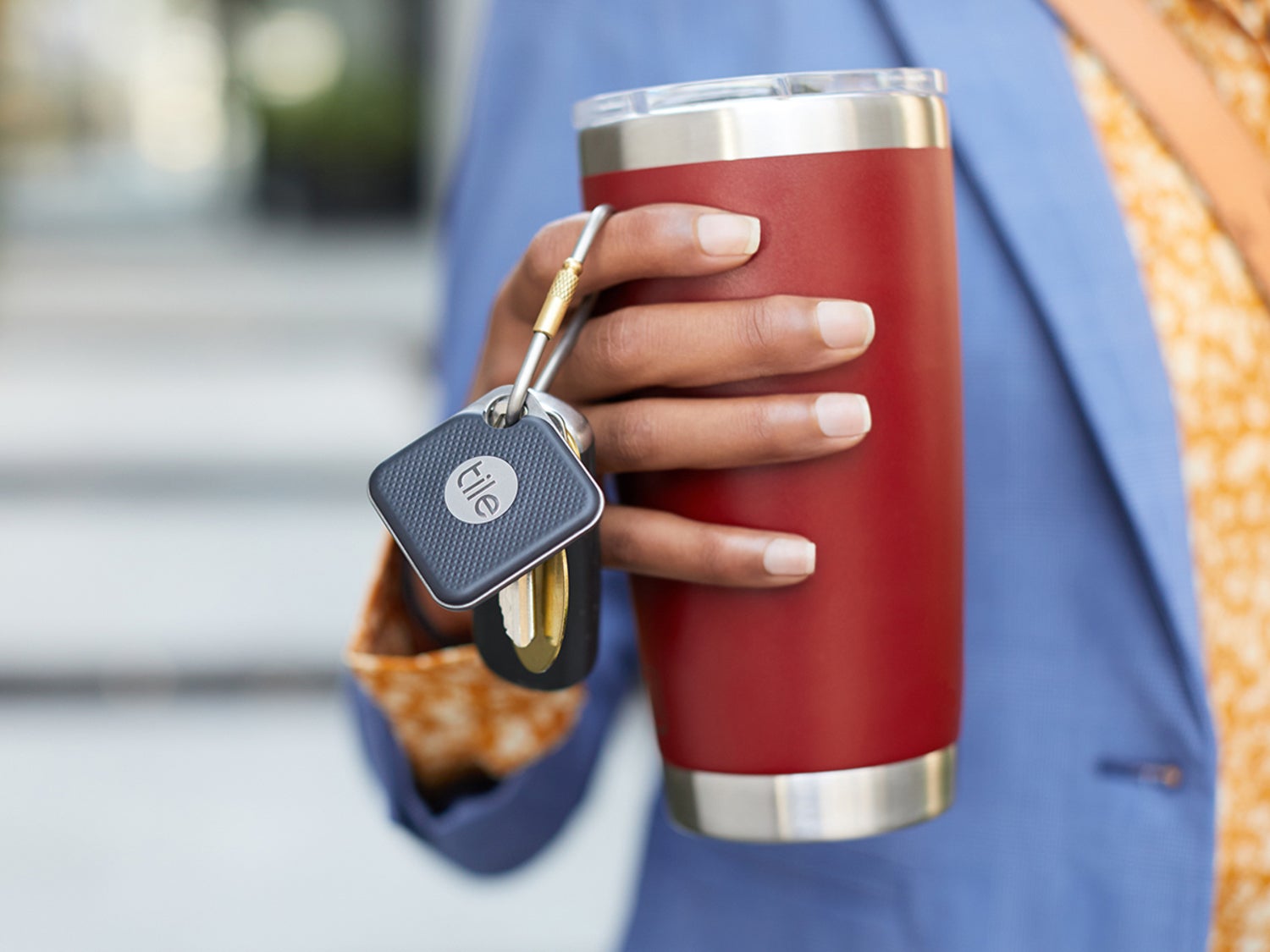 A person holding an insulated mug with a Tile tracker attached to their keys.