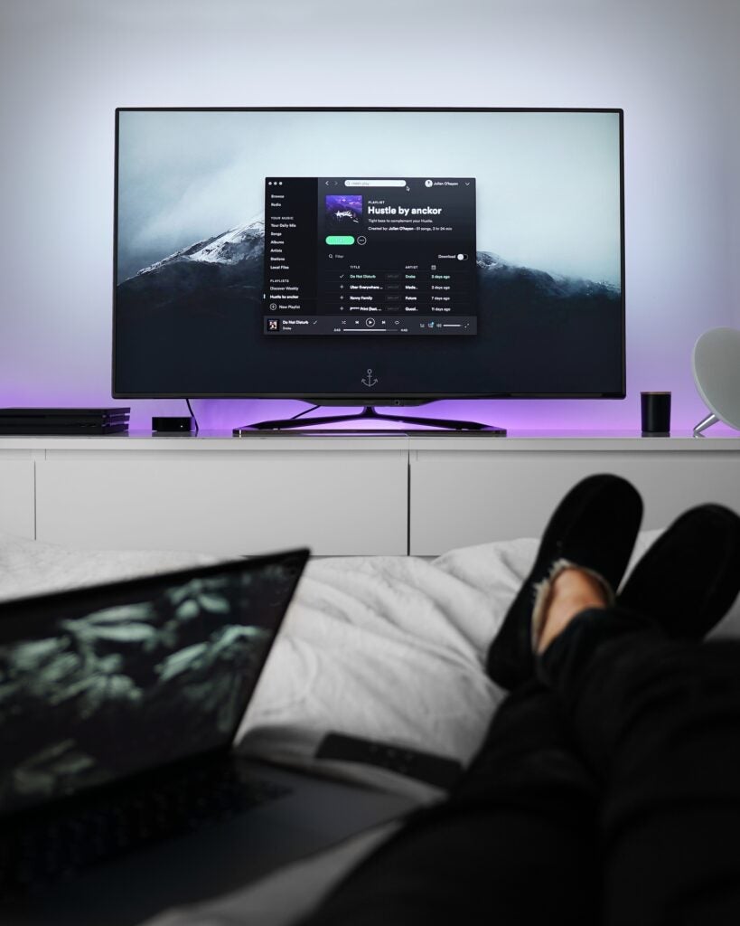 Person laying in bed streaming music from laptop to TV