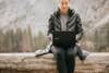 woman using laptop while sitting on a log in the wilderness in the winter