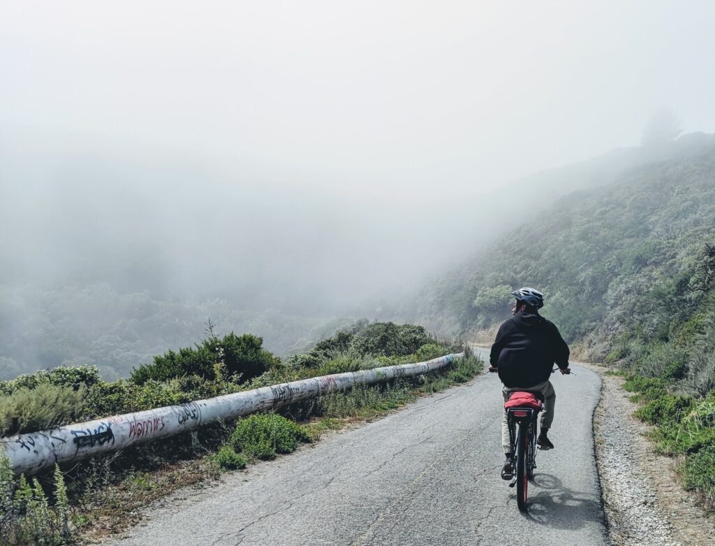 a person biking on a road in the mountains, with fog