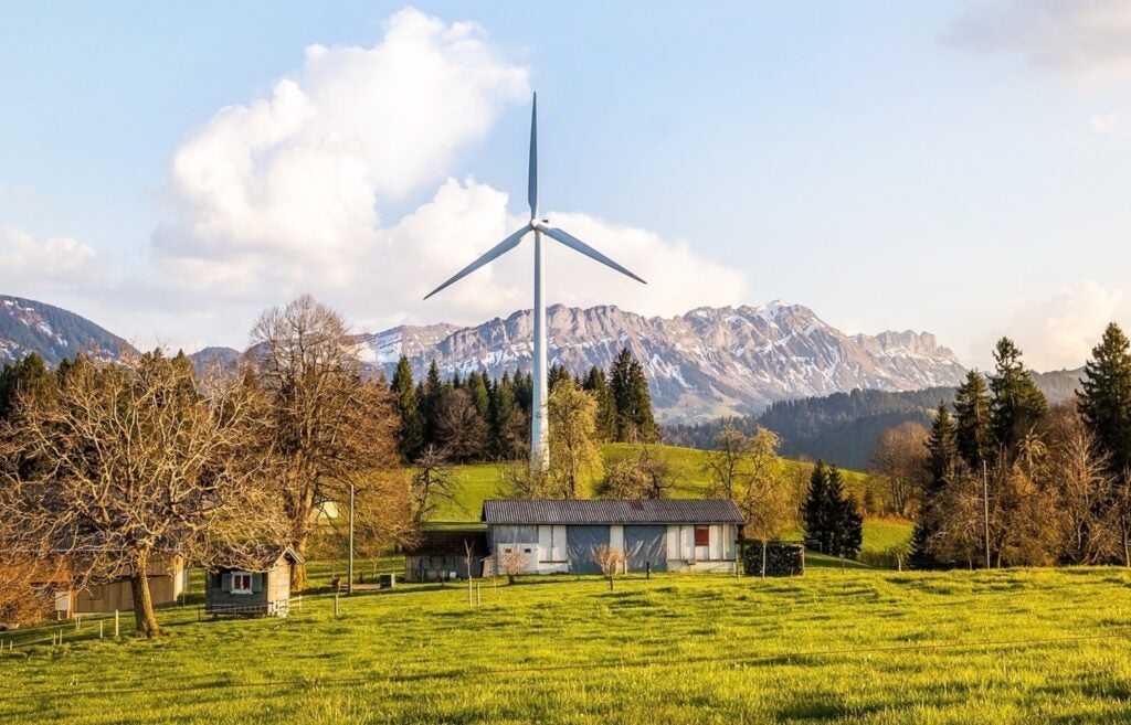 house on a green meadow with a wind turbine behind