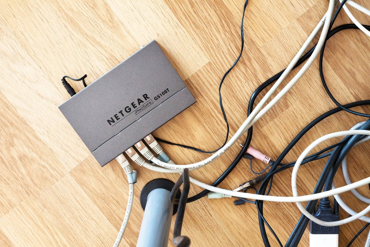 A Netgear router connected to a lot of cords, on a wood floor.
