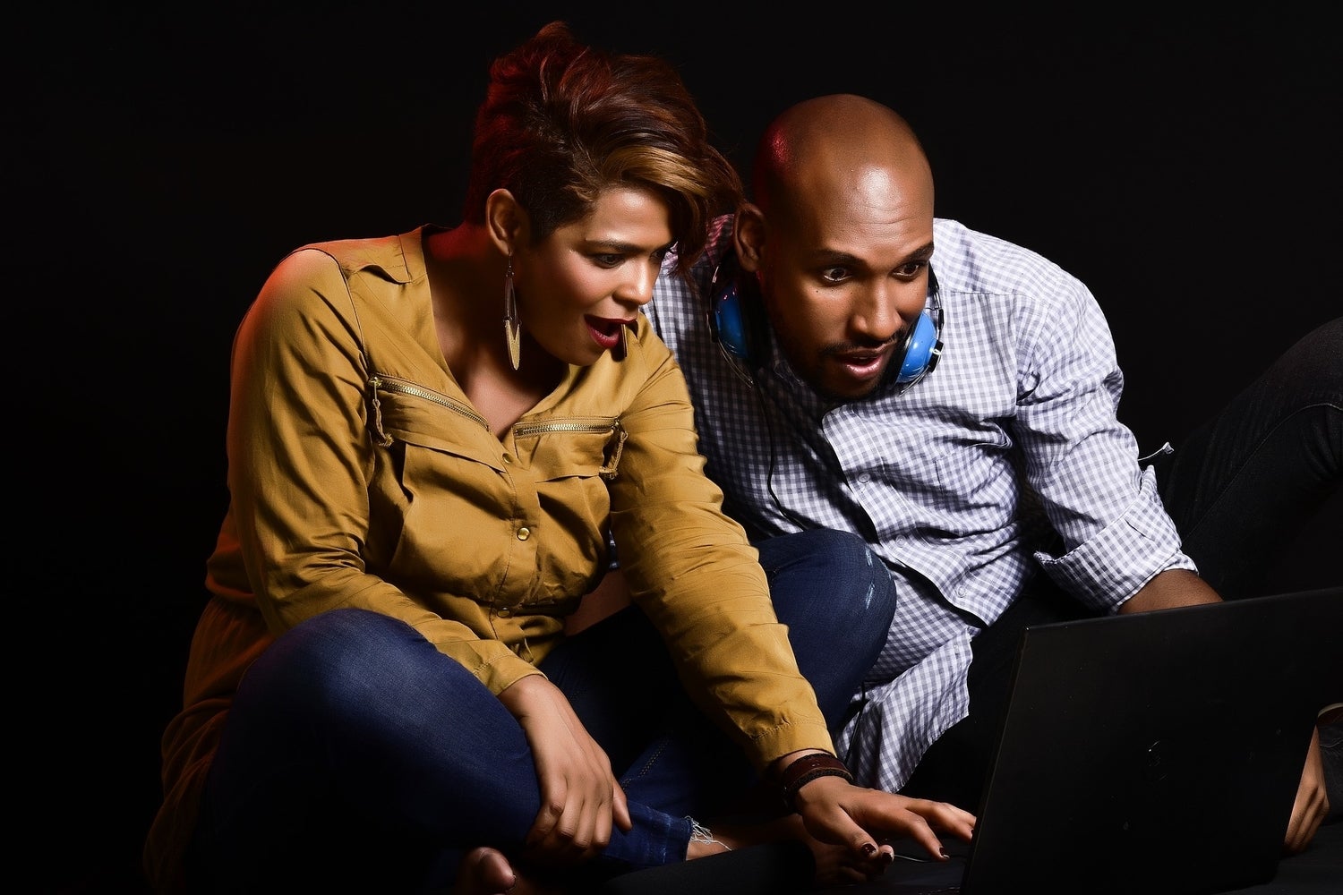 A couple looking surprised at laptop in a dark room.