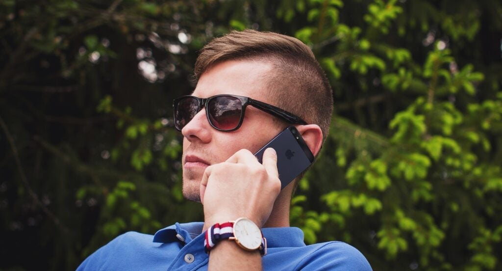 A man in sunglasses looking serious as he holds a phone up to his ear outside. This is what using a burner phone feels like.