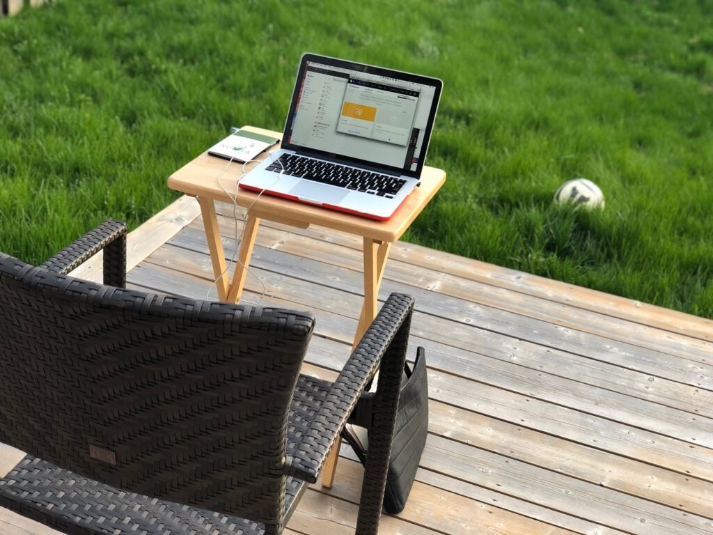 a laptop outside on a small table on a deck near a chair by the lawn