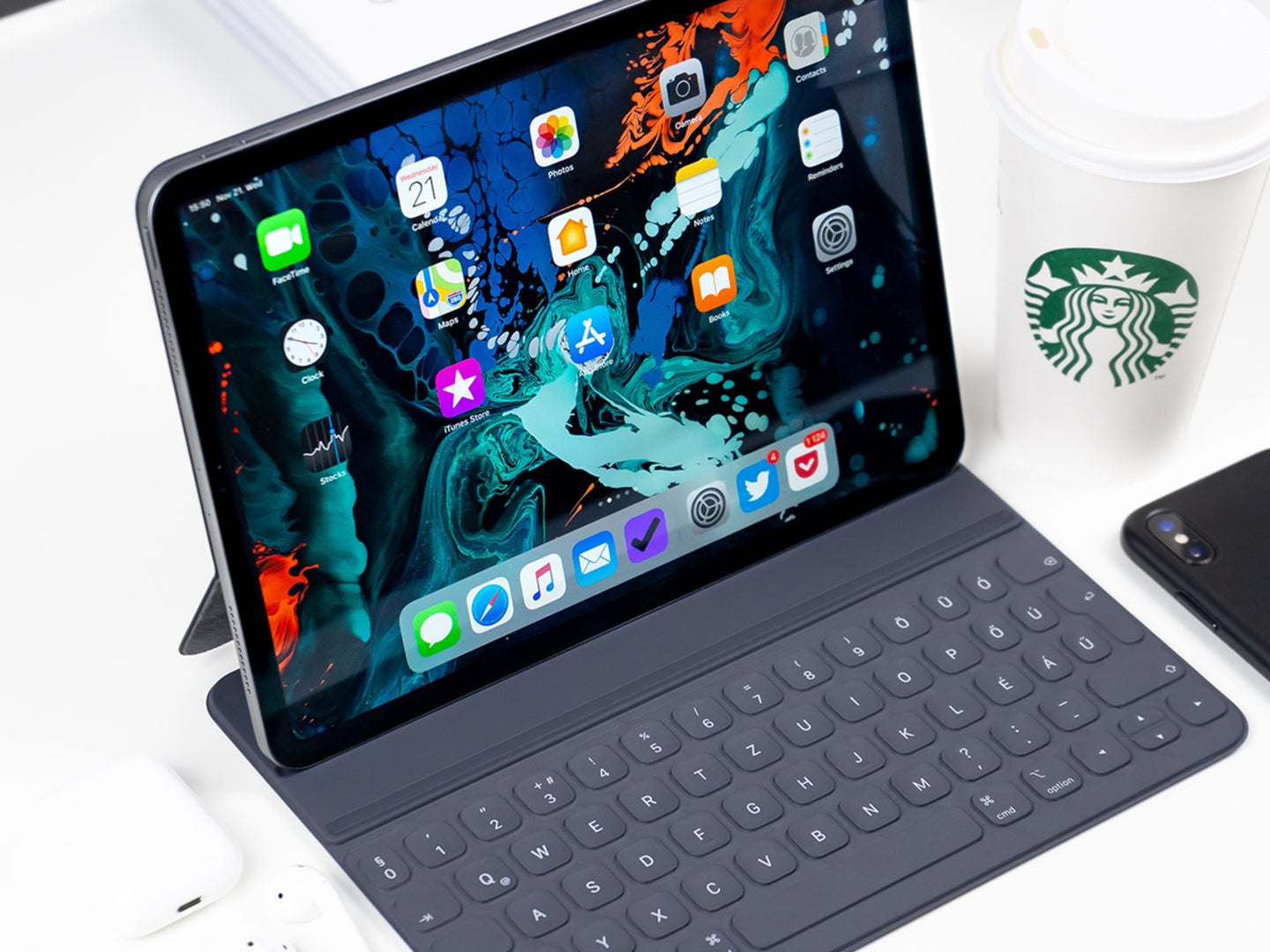 An iPad with a detachable keyboard add-on, on a white table next to a Starbucks cup and an iPhone.