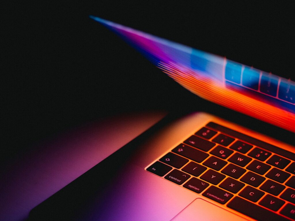 un laptop aperto con una luce rossa, arancione e viola al buio
