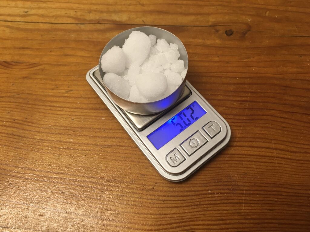 a metal container full of white powdered chemicals on a small digital gram scale