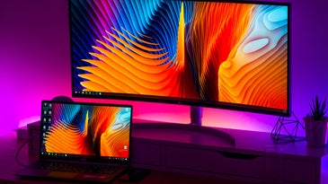 A laptop computer set up with two screens and backlit by a purple LED light.