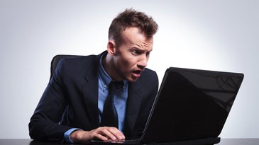 Man sitting at his laptop and looking surprised while reading something.