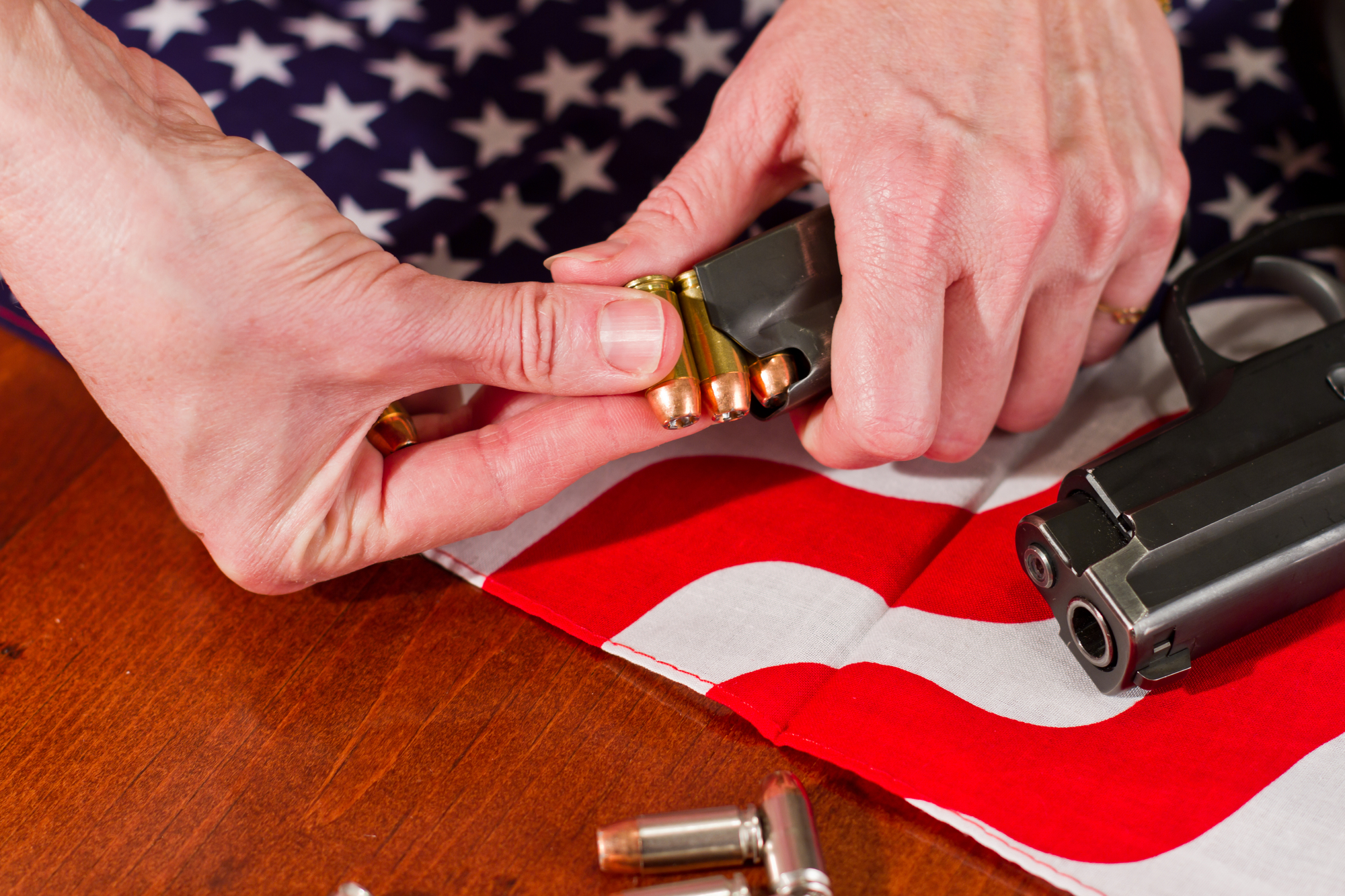 hands load a gun in front of an american flag