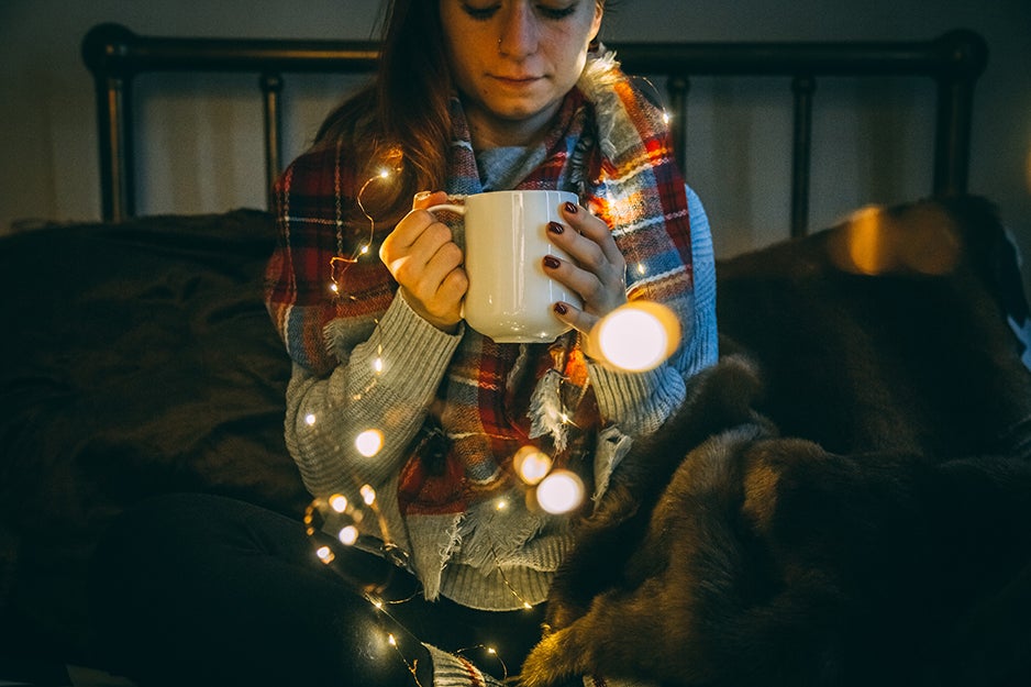 woman holding a cup wrapped in lights and a blanket