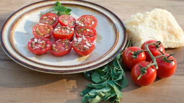 halved cherry tomatoes on a plate with marjoram, parmesan cheese, and other spices
