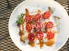 halved cherry tomatoes on a plate with parmesan cheese, marjoram, olive oil, balsamic vinegar, and other spices