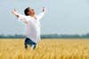 a man in a white shirt and jeans standing in the middle of a field with his arms open up to the sky