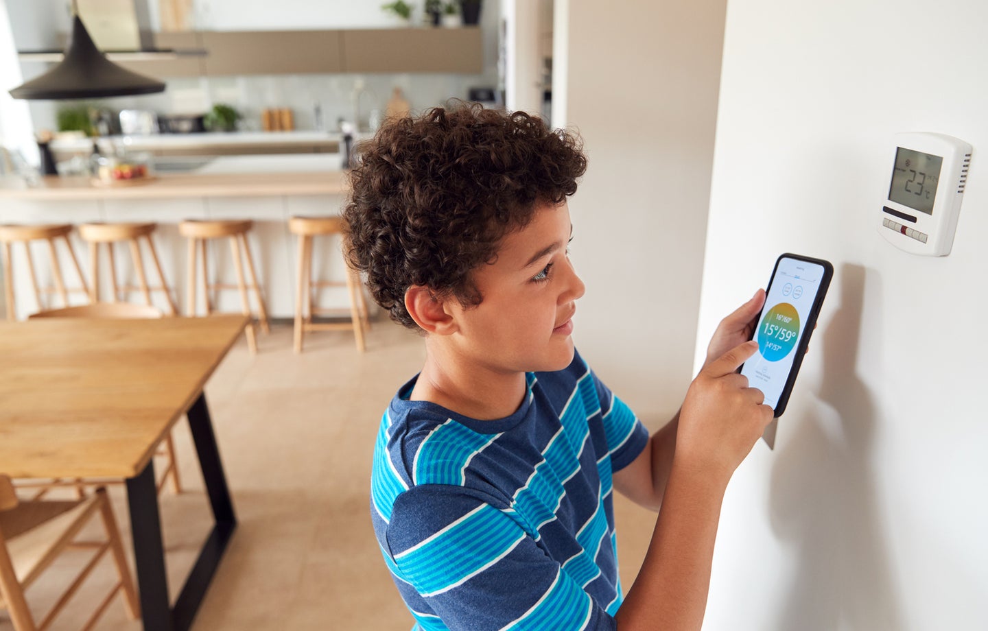 Boy Changes Temperature On Central Heating Thermostat Control Using Mobile Phone App