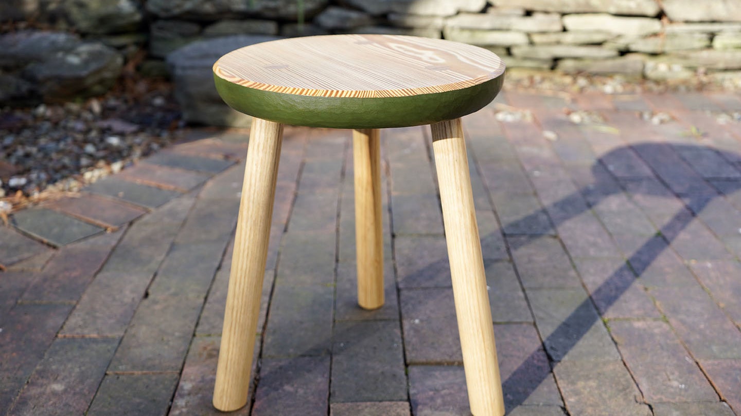 a wooden three-legged stool on a brick patio