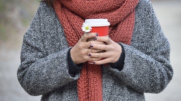 woman with a scarf around neck and coffee in hands