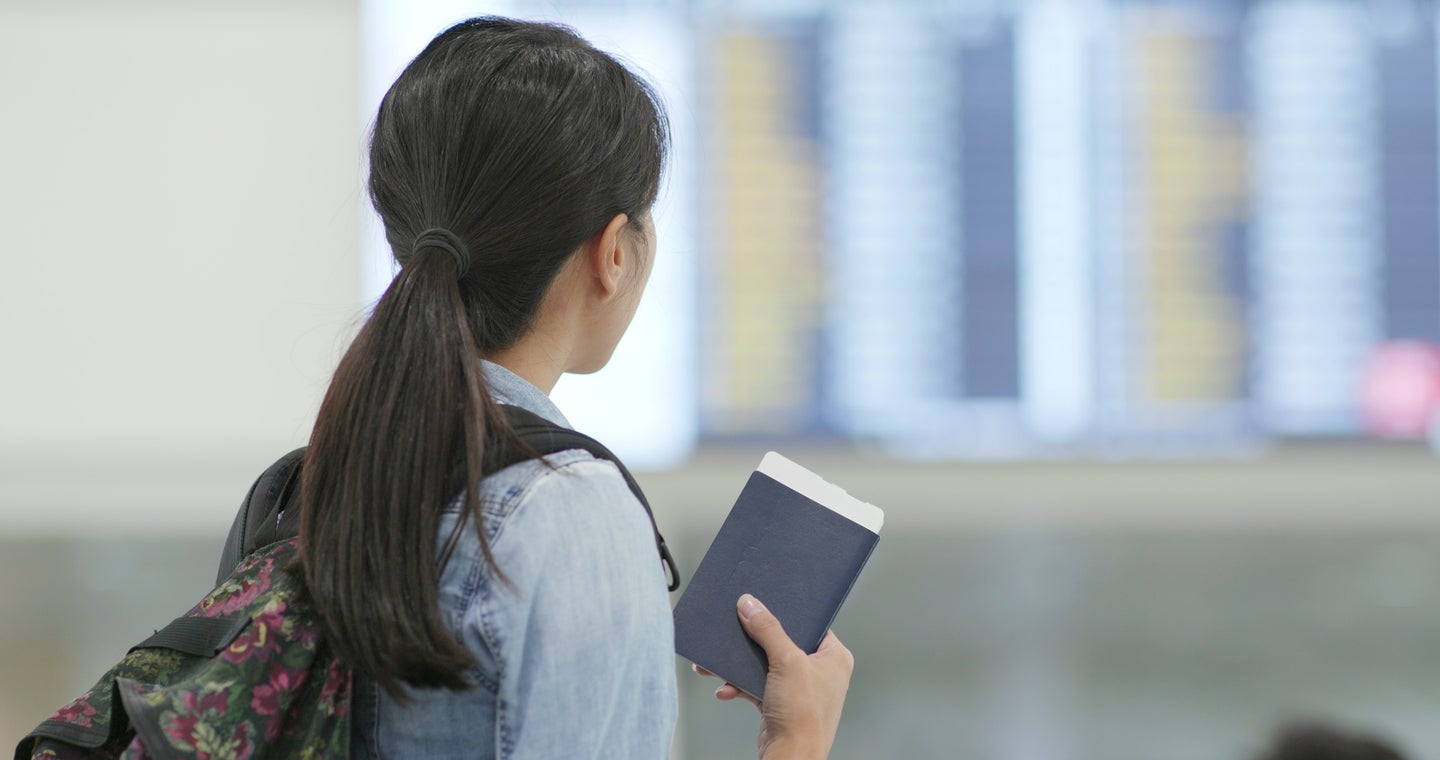 A young asian woman stands in an airport holding a passport