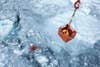 person in crane basket with rope attached to measuring instruments in icy water