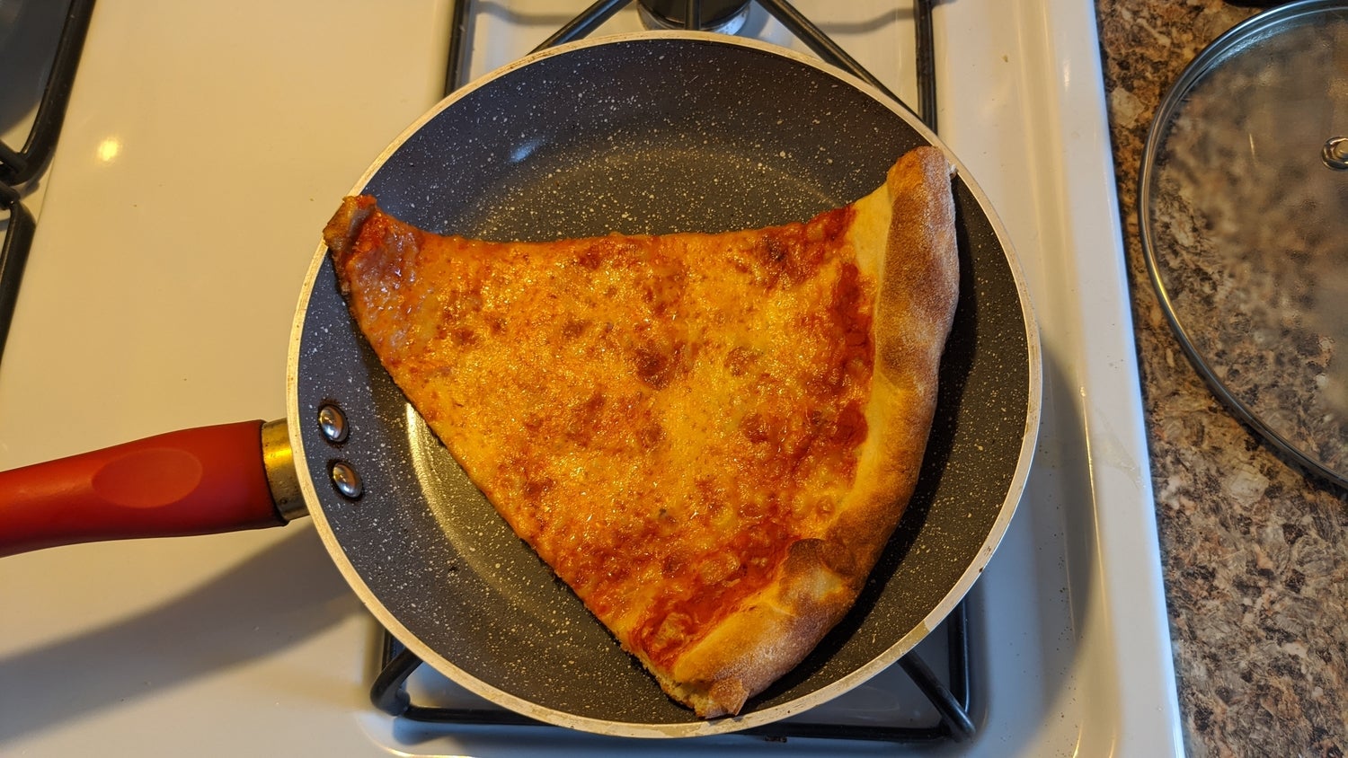 A slice of cheese pizza in a frying pan as part of an experiment to find the best way to reheat pizza.