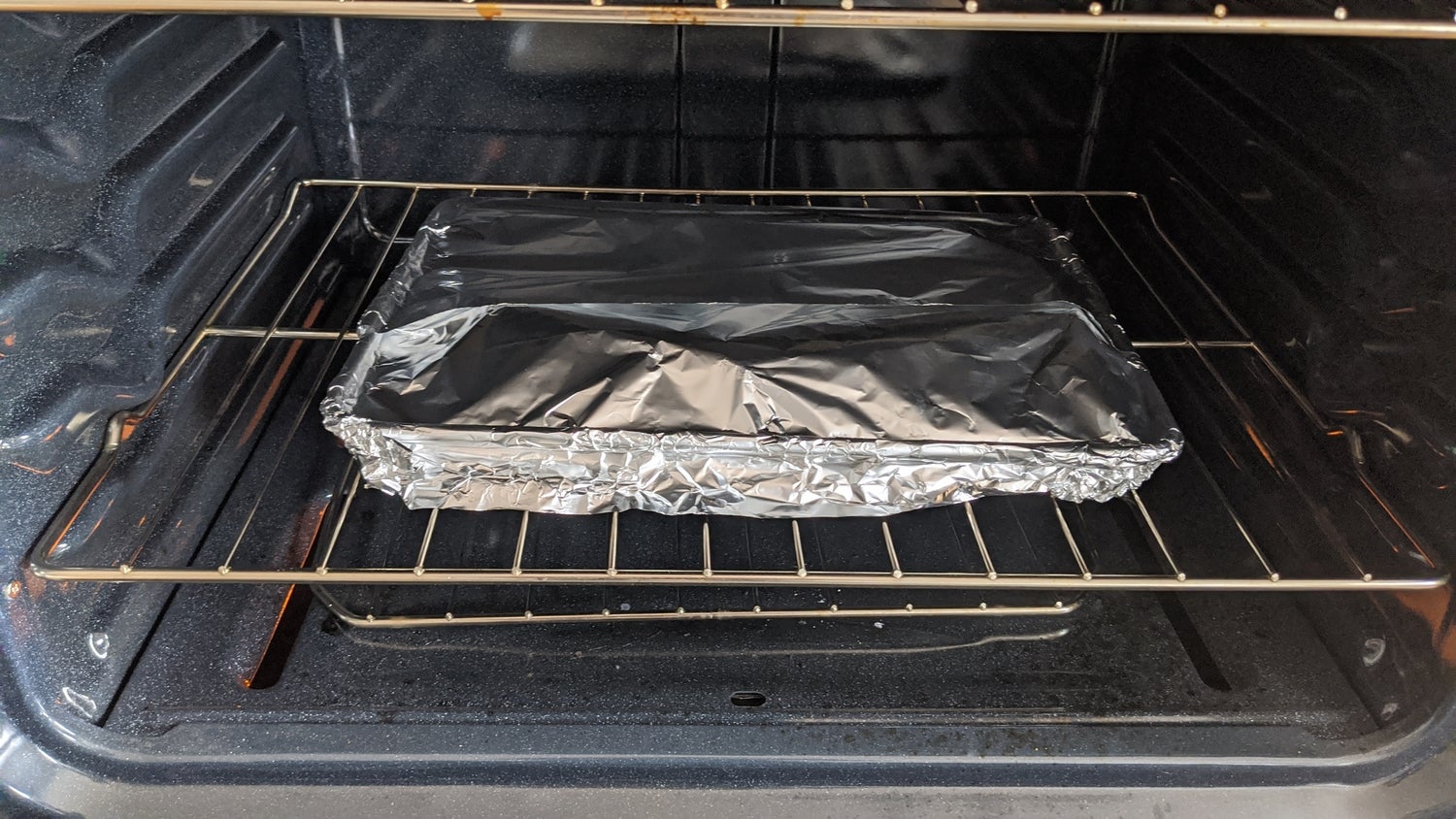 A tray of pizza covered with aluminum foil inside an oven.