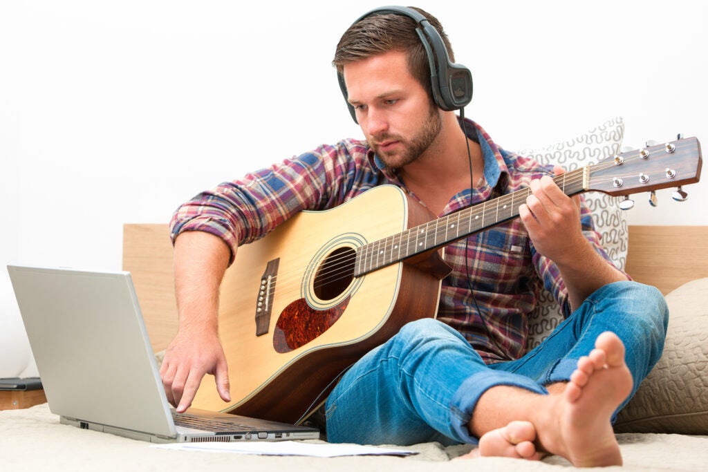 Person on sofa playing the guitar with laptop at home