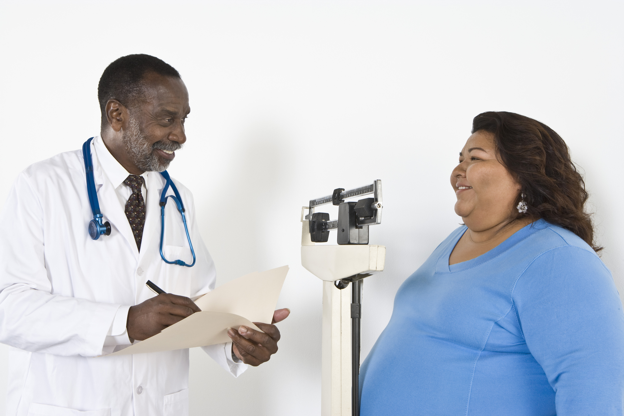 a doctor smiles at a patient while reading her weight off a scale