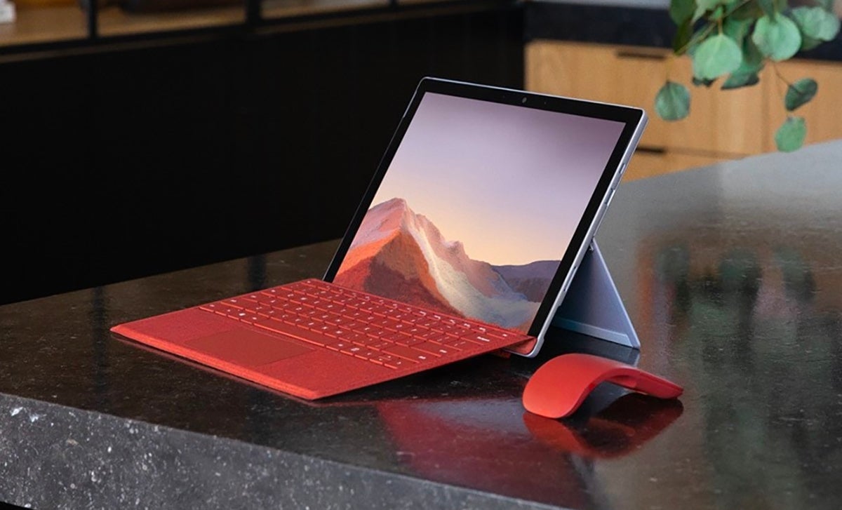 A Microsoft Surface tablet with a red keyboard and mouse on a shiny black countertop.