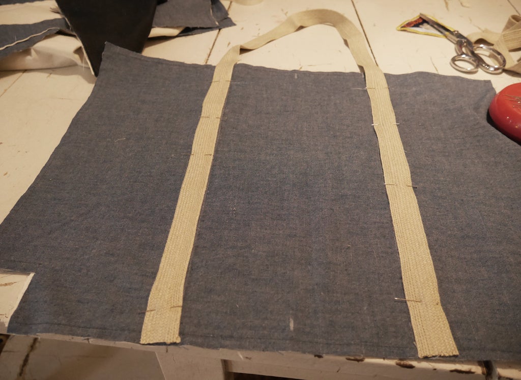 the webbing handles of a DIY zippered tote bag made out of leftover fabric scraps, pinned in place