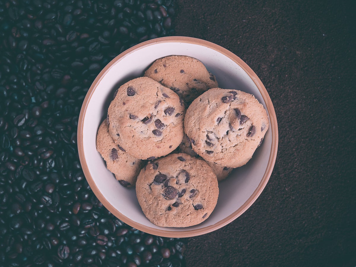 a bowl of chocolate chip cookies on a bed of whole coffee beans and ground coffee