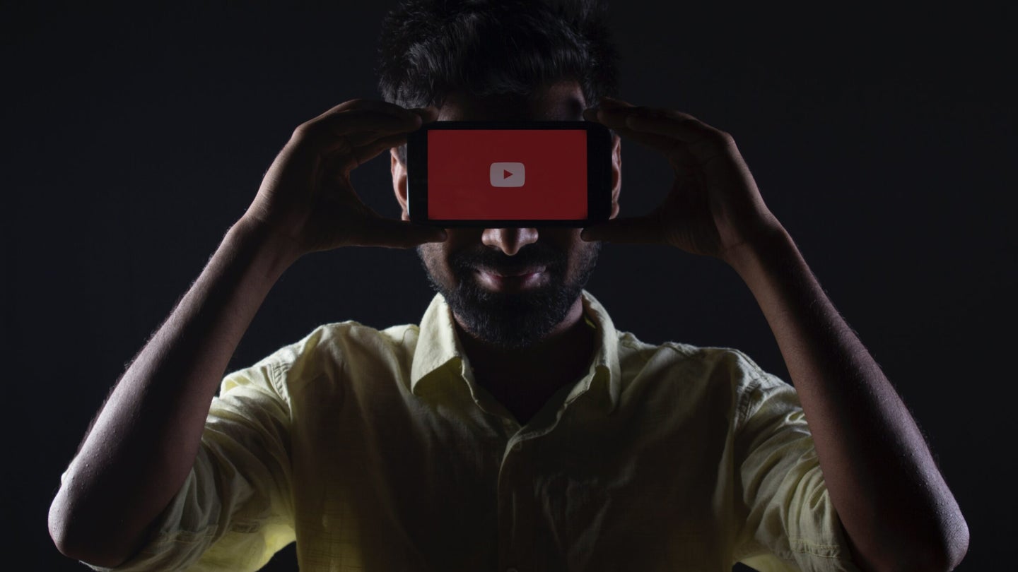 A man holds a smartphone with the YouTube app.