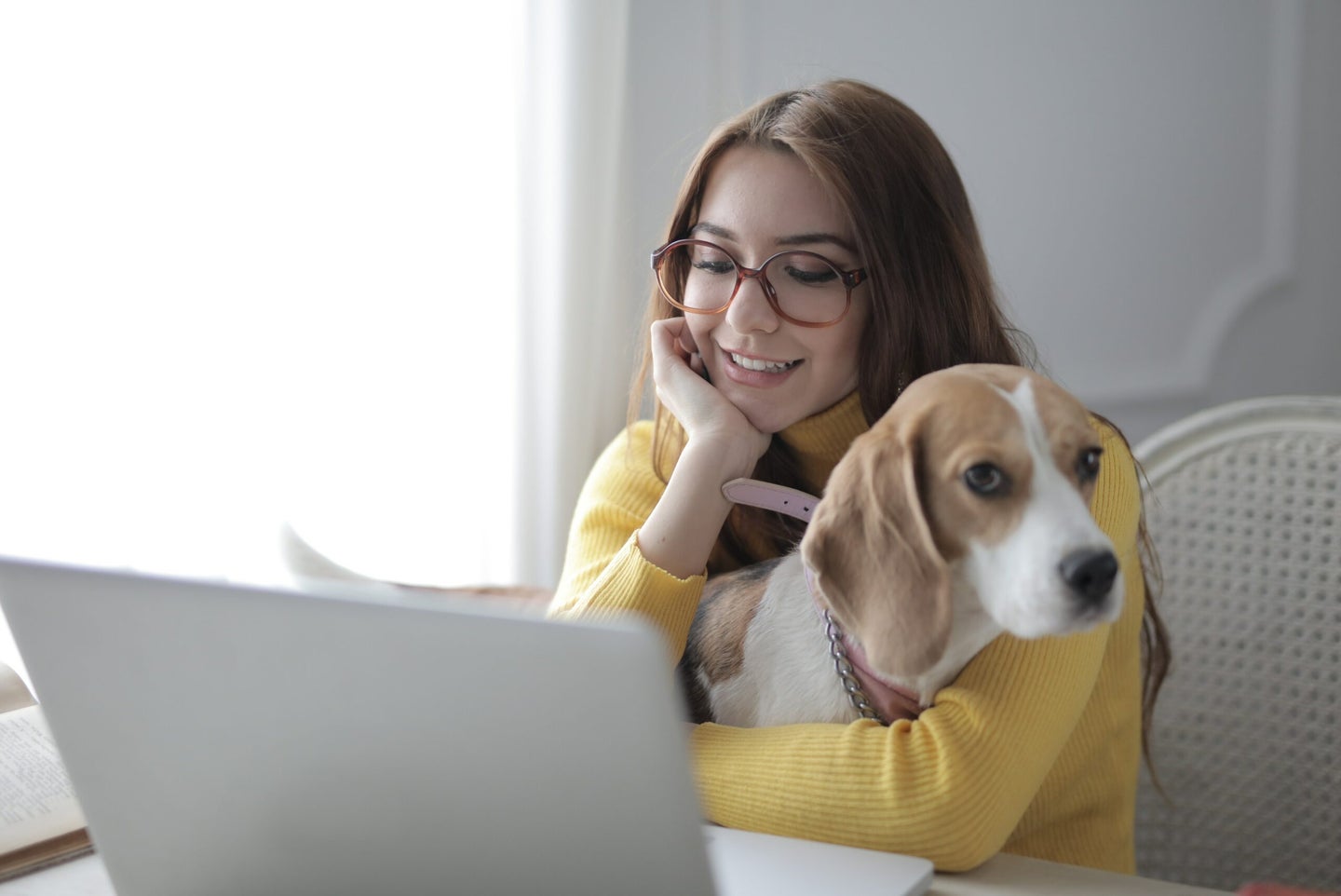 A woman smiling at her computer and holding a dog