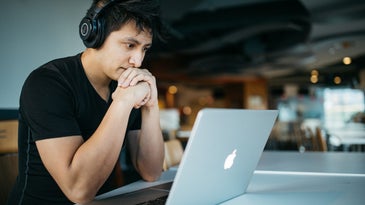 Worker sitting at Mac laptop with wireless headphones on