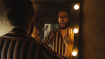 A man standing at a mirror and yelling at his reflection in the dark.