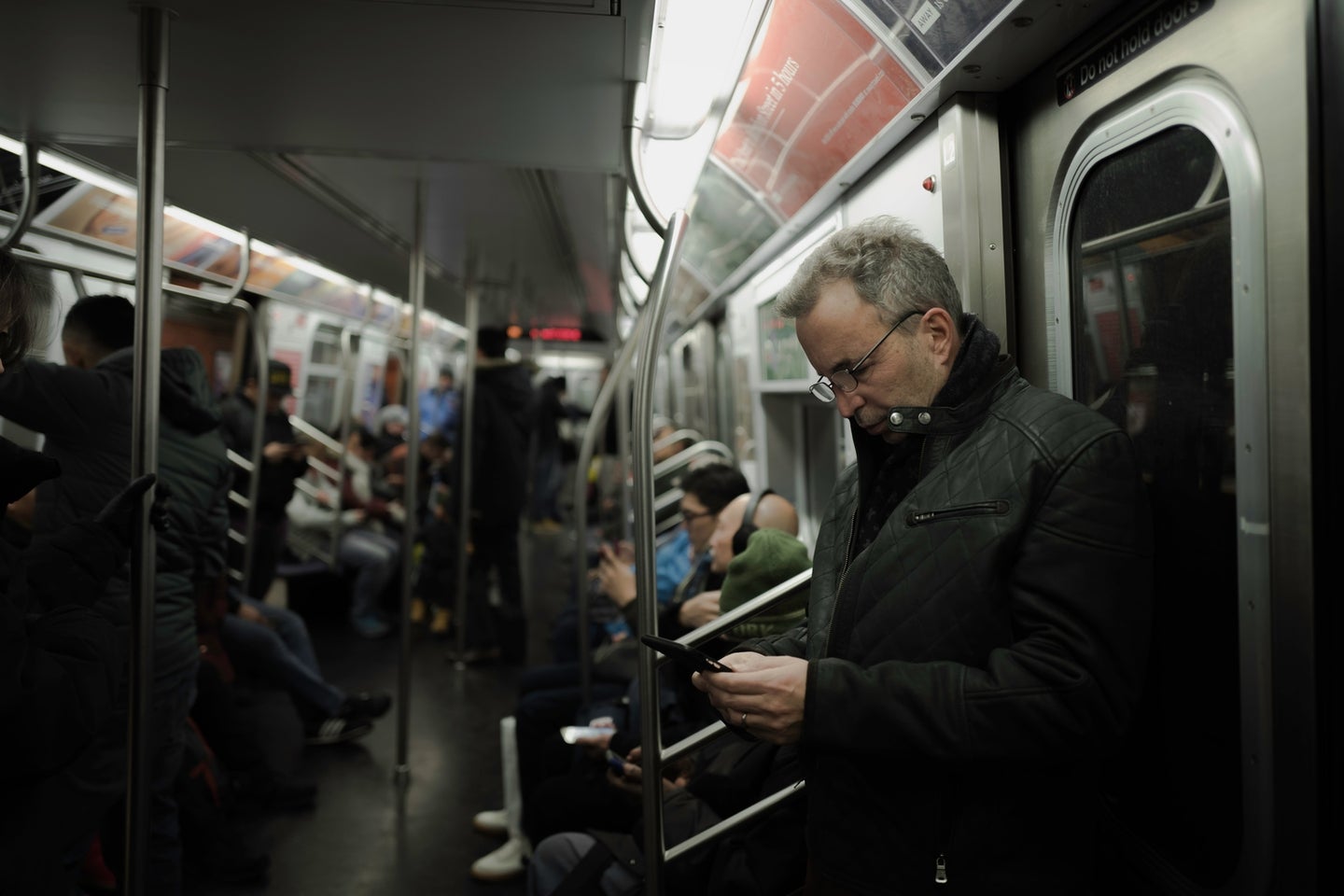 a man using his phone on the New York City subway, while other passengers also use their phones