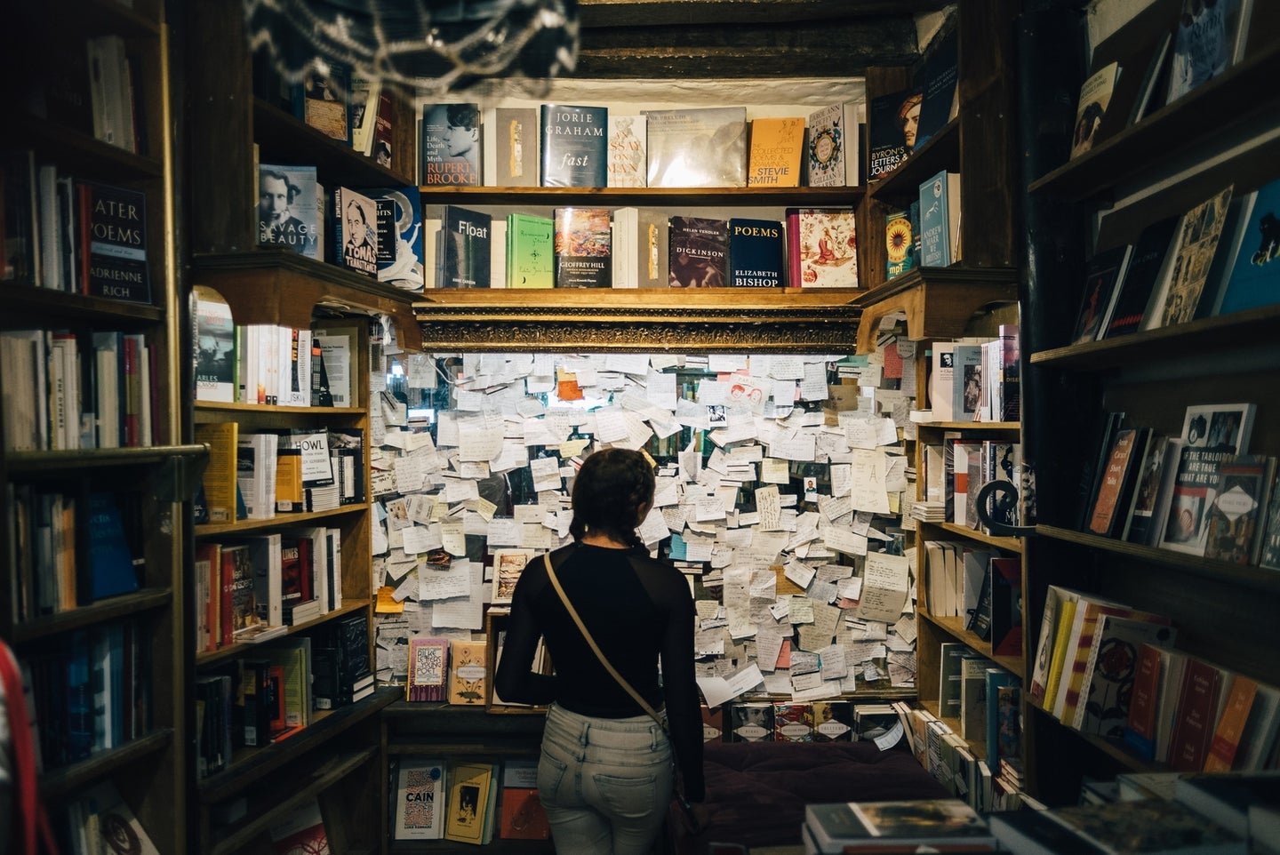 a person standing in front of a wall with a lot of notes on it, surrounded by books