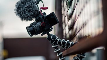 A black professional camera hanging over a wooden fence.