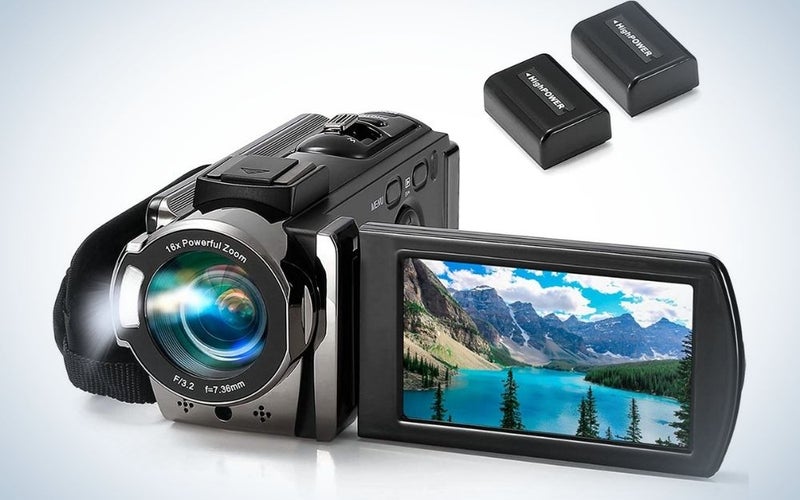 A black and silver professional camera with a small desktop with a mountain view in it and with two high power black batteries.